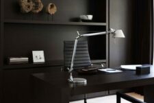 a minimalist home office with matte black walls and built-in shelves, a black desk and comfortable chairs