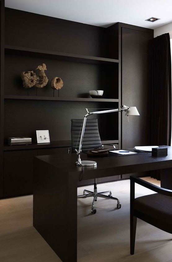 a minimalist home office with matte black walls and built-in shelves, a black desk and comfortable chairs