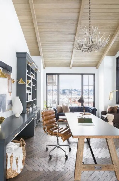 a modern rustic home office with a large graphite grey storage unit, a wooden desk, a leather chair and an antler chandelier