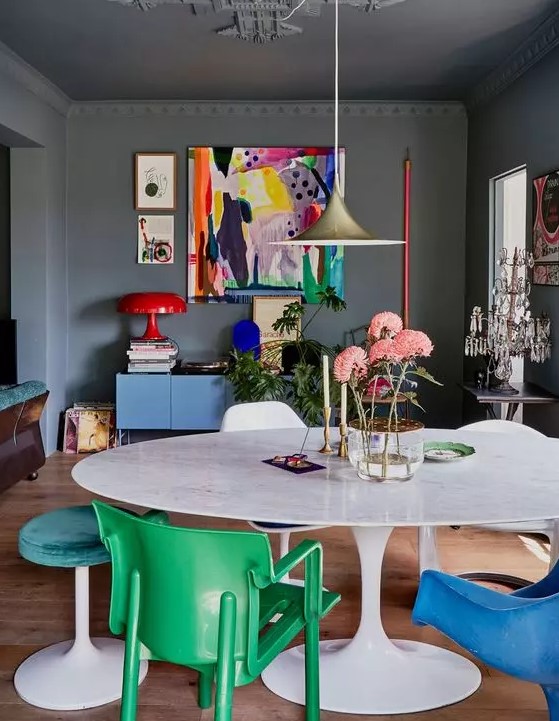 a moody home office made bright with furniture and artwork, with green and blue chairs and stools, a blue dresser, a colorful artwork and a red lamp is a lovely space