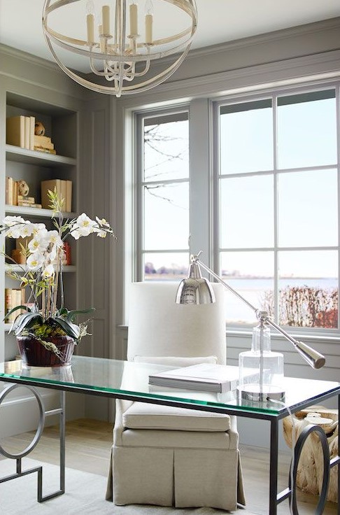 a neutral and super elegant home office in light grey, a glass desk, a white chair, a farmhouse chandelier and a cool view