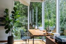a peaceful home office with a glazed wall and a corner window, a sleek desk, a black chair, a floor lamp and a view to the greenery