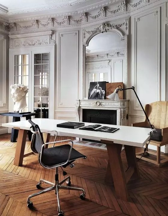 a refined and chic Parisian-inspired home office with molding, a fireplace, a stained chair, a black table, a large desk and a cool lamp