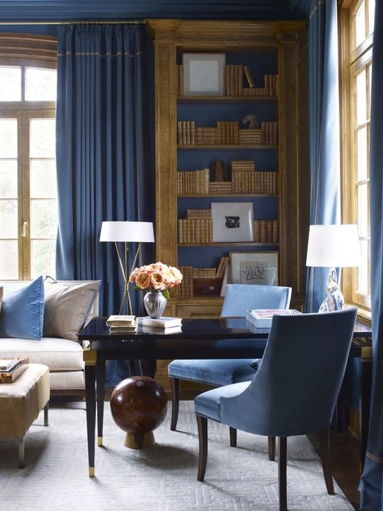 a refined blue home office with a chic black desk, blue chairs, walls and textiles and elegant touches of gold here and there