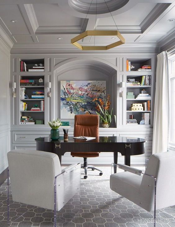 a refined grey home office with dove grey walls, a built-in storage unit, a dark-stained desk, white chairs and a hexagon chandelier