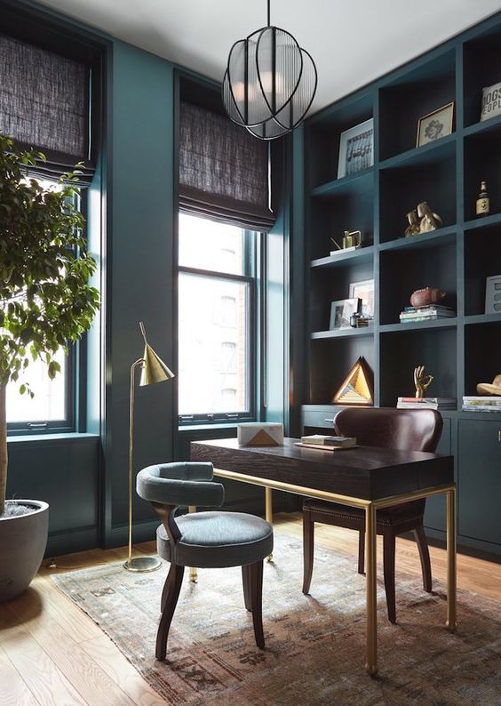 a refined teal home office with a built in storage unit, a dark stained desk and a brown chair, a grey chair and gilded touches