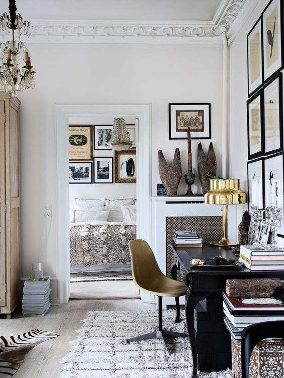 a sophisticated home office with a refined black desk, a neutral chair, a gallery wall, a bit of artworks and a crystal chandelier