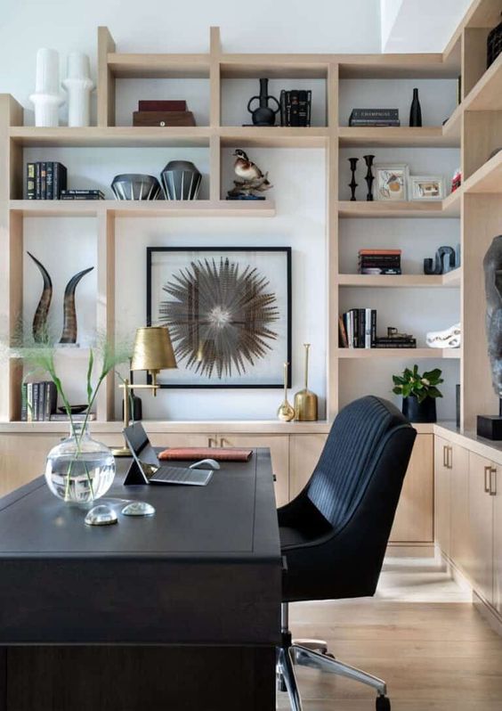 a stylish home office with a black desk and a chair, light-stained cabinets and shelves, gilded touches and artwork