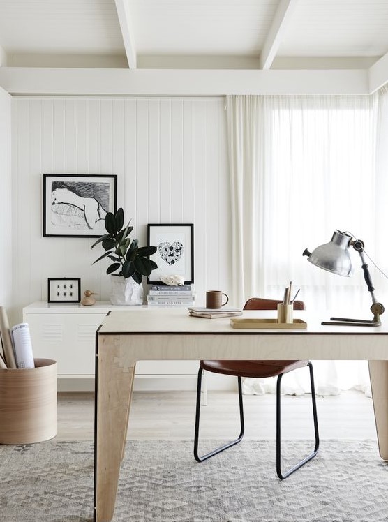 a stylish neutral home office with a plywood desk, a cabinet on the wall, a leather chair, some artworks