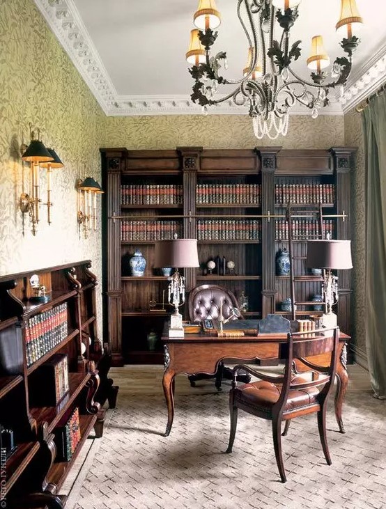 a vintage home office with dark-stained bookcases and bookshelves, a dark-stained desk and leather chairs, table and wall lamps and a cool chandelier