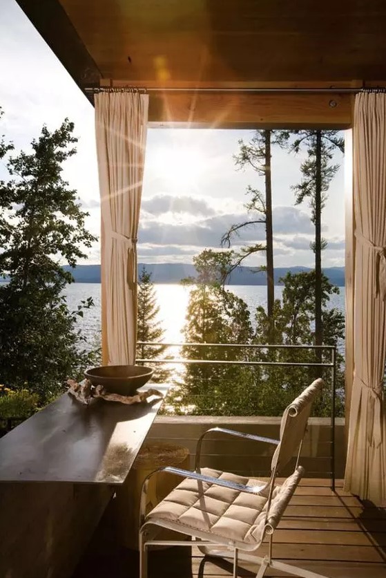 an adorable home office with glazed walls, jaw-dropping views of the lake, a metal desk and a comfy chair is a lovely space to enjoy the views and get inspired