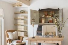 an exquisite vintage home office done in neutrals, with a bureau, a desk, a beige and a creamy chair floating shelves and a stack of books