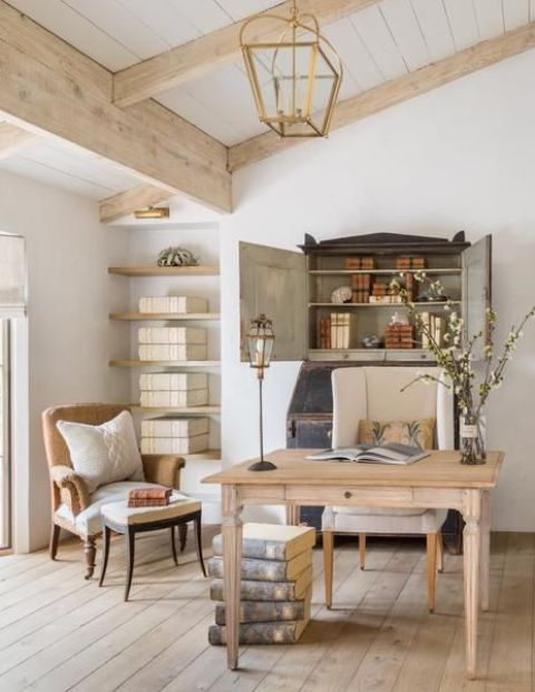 an exquisite vintage home office done in neutrals, with a bureau, a desk, a beige and a creamy chair floating shelves and a stack of books