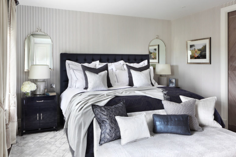 a luxurious vintage-inspired bedroom with pinstripe walls and a stunning navy blue upholstered emperor bed, grey and navy textiles and accessories