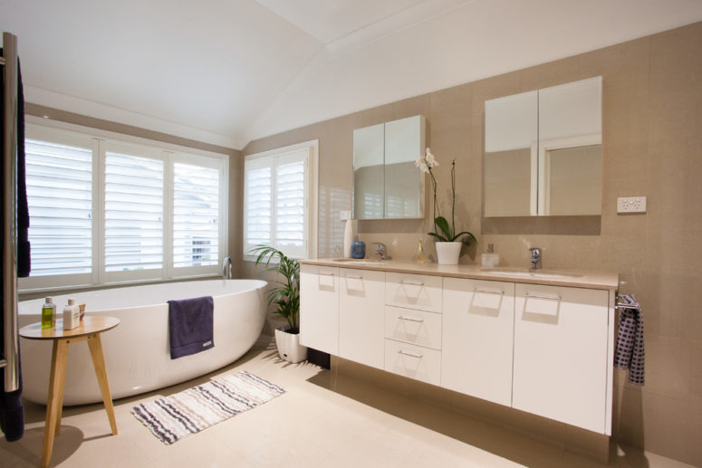 a taupe and creamy bathroom with layered rugs, potted greenery and a window with shades to keep privacy (Urban Design Solutions)