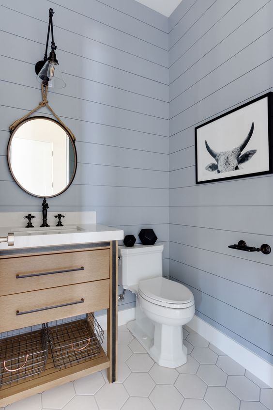 a beautiful contemporary light blue powder room, a wooden vanity, hex tiles on the floor and a mirror hanging on rope