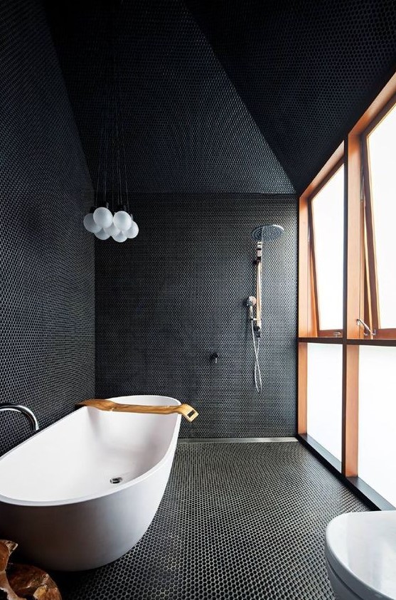 a black bathroom fully clad with penny tiles with white grout, with a frosted glass wall and a free-standing bathtub