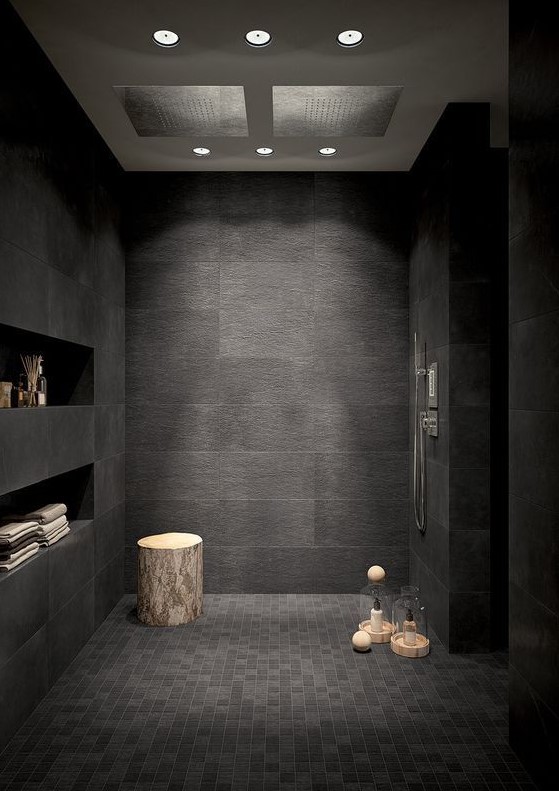 a black bathroom with large and smaller scale tiles, built-in shelves and a tree stump table