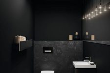 a black powder room with matte black walls, white appliances, a cluster of bulbs hanging down and some built-in lights