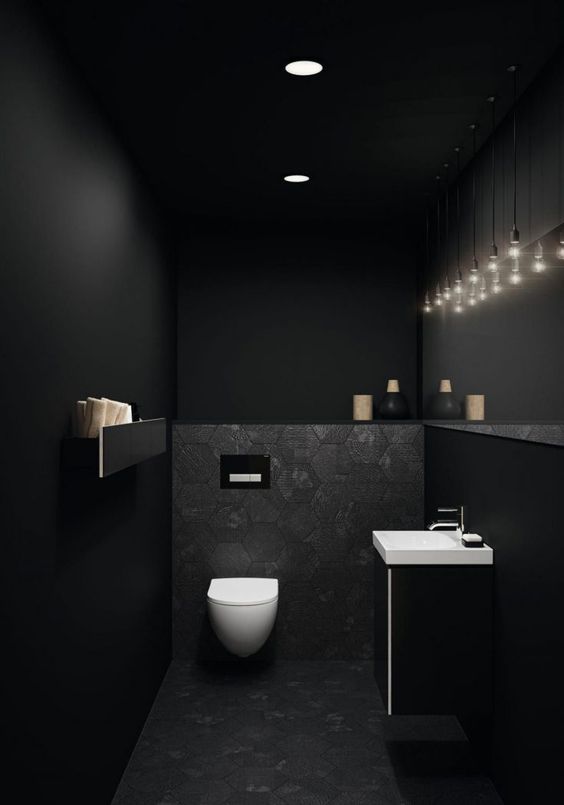 a black powder room with matte black walls, white appliances, a cluster of bulbs hanging down and some built-in lights