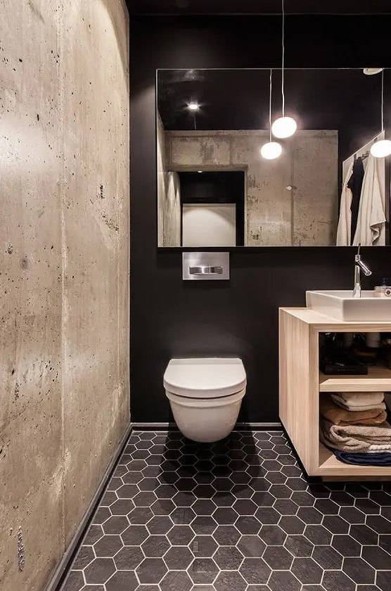 a black wall, black hex tiles and a contrasting concrete wall for a modern bathroom with an industrial feel