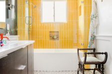 a bold bathroom with yellow skinny tiles, a printed tiled floor, a bright rug, vintage dark-stained furniture, floral towels is amazing