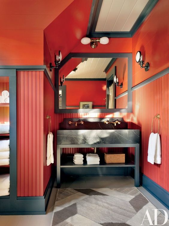 a bold farmhouse bathroom with red walls, graphite grey touches and a large mirror plus a printed rug