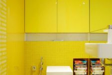 a bold yellow powder room clad with small scale yellow tiles, with bright glossy yellow cabinets and a mirror wall is a chic spot