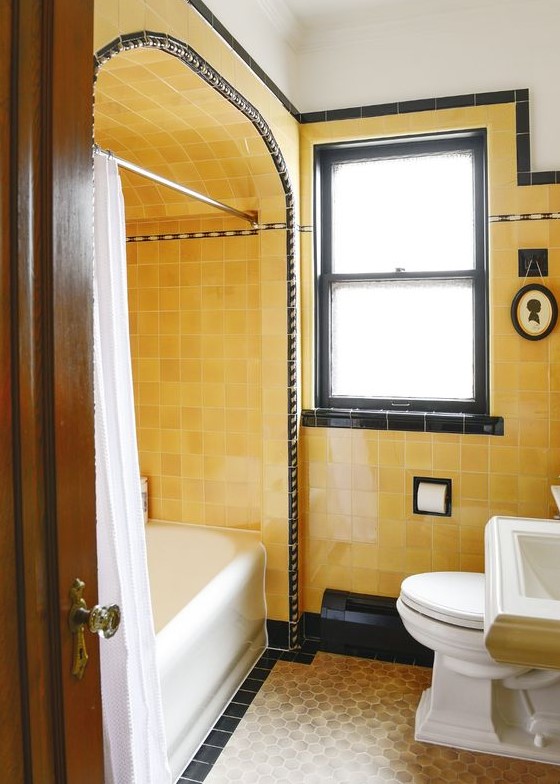 a bright vintage bathroom with yellow tiles, black touches for drama and white vintage appliances