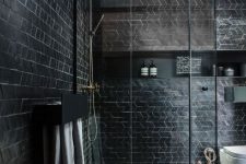 a catchy modern black bathroom with geo clad tiles, a niche shelf and a shower enclosed in glass is cool