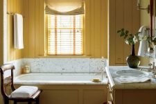 a charming vintage bathroom with mustard beadboard walls, a vanity and a bathtub clad with mustard wood and neutrals