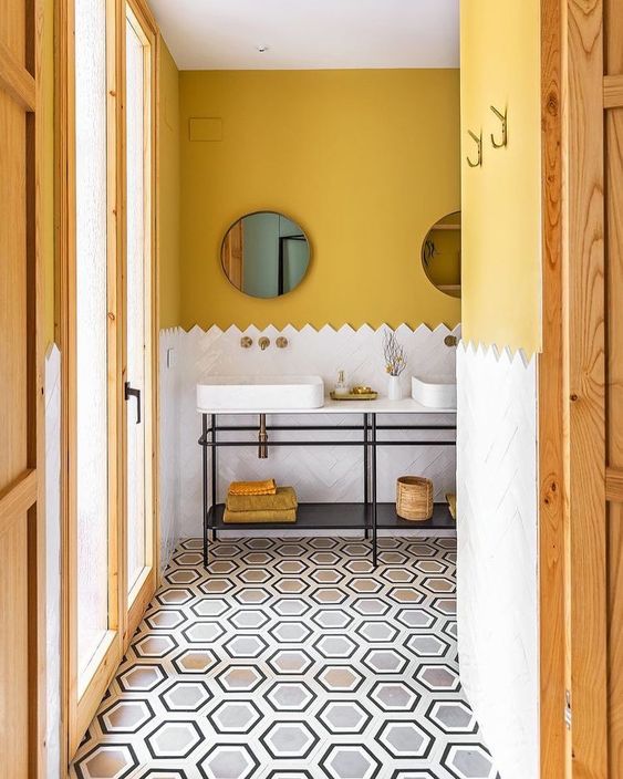 a chic bathroom with mustard walls, white herringbone tiles, a double vanity with bowl sinks and round mirrors