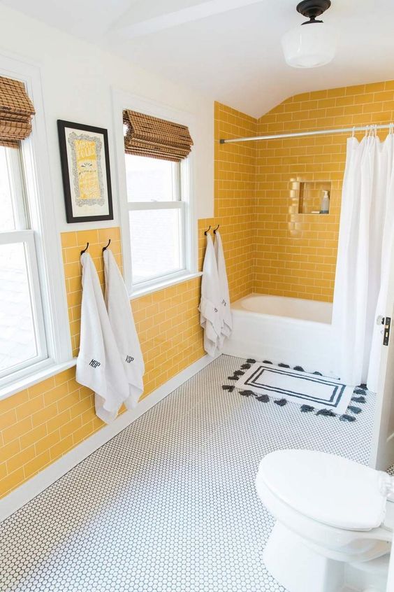 a chic bathroom with sunny yellow walls, penny tiles on the floor, black and white textiles and woven shades on the windows