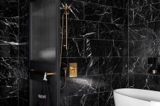 a chic black and gold bathroom with black marble tiles, black fixtures, a black space divider and a white tub