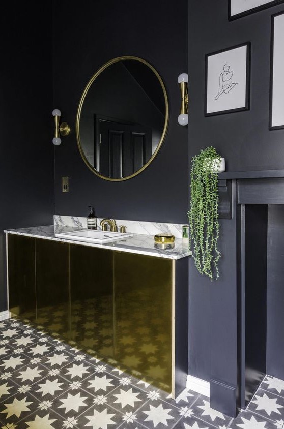a chic black and gold bathroom with matte black walls, a polished gold vanity, gold fixtures and lamps and a mosaic floor