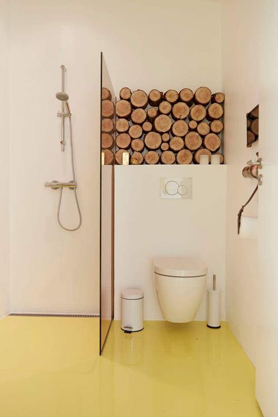 a chic minimalist bathroom with neutral walls and a pale yellow floor, neutral appliances and a stack of firewood for decor