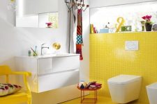 a colorful bathroom with a yellow tile wall and floor plus a chair and all white around looks quirky and cool
