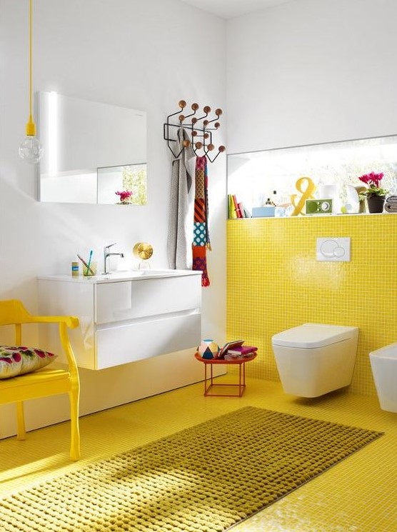 a colorful bathroom with a yellow tile wall and floor plus a chair and all white around looks quirky and cool