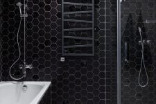 a contemporary bathroom with black hex tiles, a mosaic tile floor, a shower enclosed in glass and a black radiator