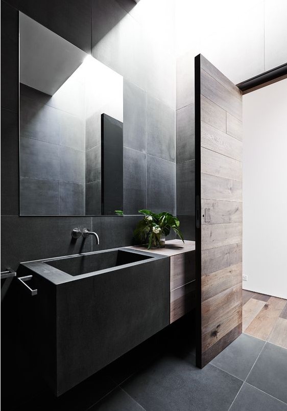 a contemporary black bathroom done with large scale tiles, a box matte black sink and some rich-stained wood