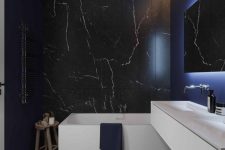 a contemporary black bathroom with black marble tiles, a white vanity and white appliances, built-in lights