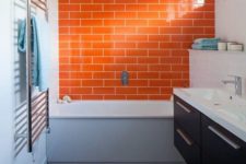 a contrasting grey and white bathroom is accented with a dark stained floating vanity and a bright orange tile wall