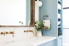 a cozy rustic bathroom with light blue furniture, a wooden frame mirror and brass fixtures