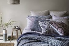 a dove grey bedroom with layered navy blue and blue bedding and a wicker lampshade