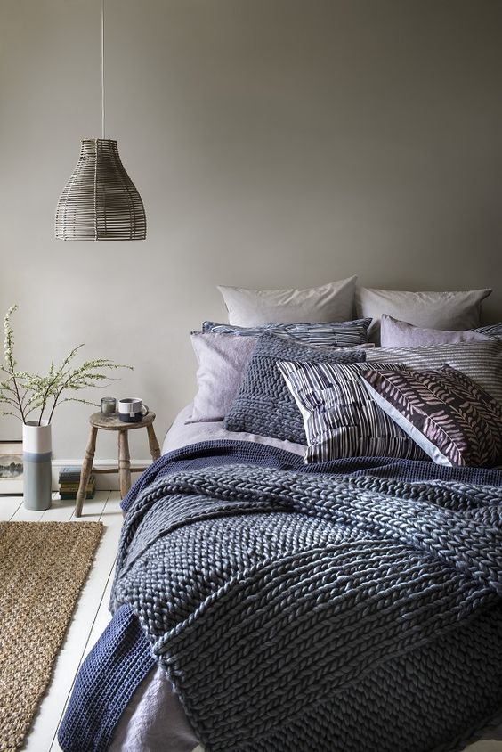 a dove grey bedroom with layered navy blue and blue bedding and a wicker lampshade