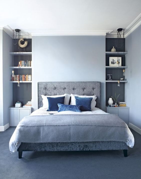 a light blue bedroom with grey niches, a grey upholstered bed and floor plus bold blue accents