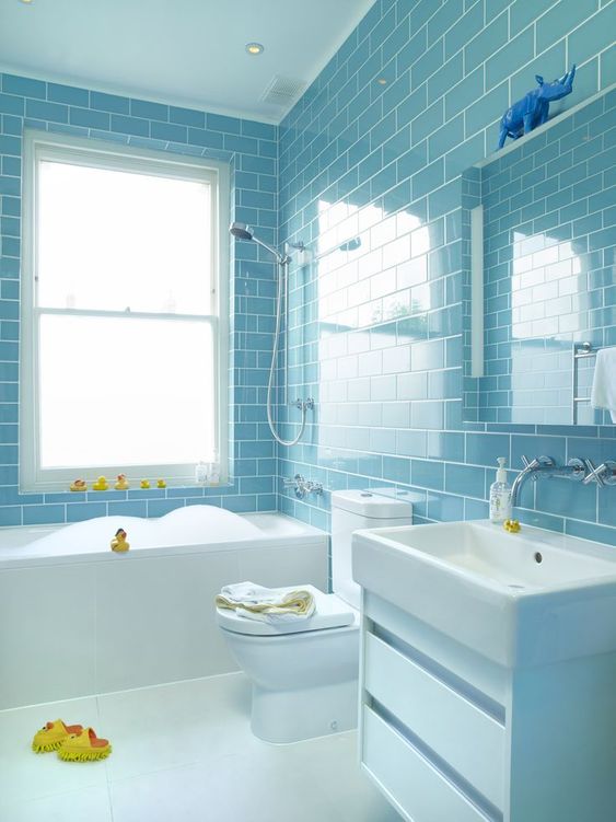 a light blue subway tile clad bathroom with white fixtures and appliances, yellow ducks for fun