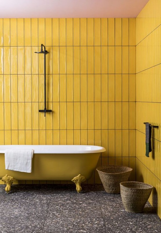 a minimal bathroom with mustard tile walls and a mustard bathtub, a dark stone tile floor and baskets
