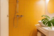 a minimalist bathroom clad with white tiles, with wooden beams on the ceiling and a sunny yellow tile wall