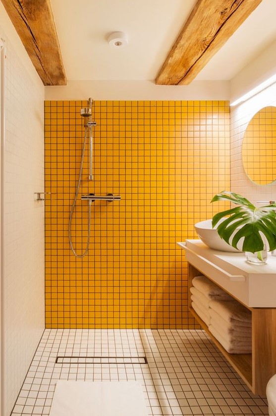 a minimalist bathroom clad with white tiles, with wooden beams on the ceiling and a sunny yellow tile wall
